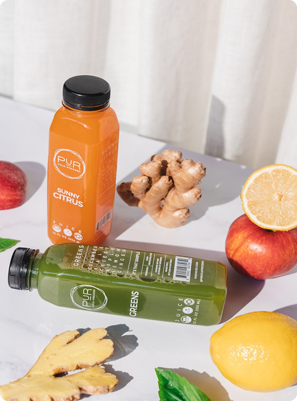 PUR Sunny Citrus and Greens juices with lemon, apple, ginger and basil on a sunlit table.