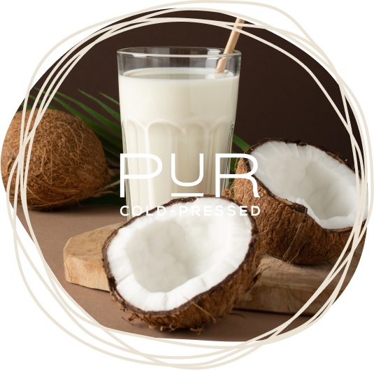 Glass of coconut milk surrounded by raw coconuts on a wooden board.