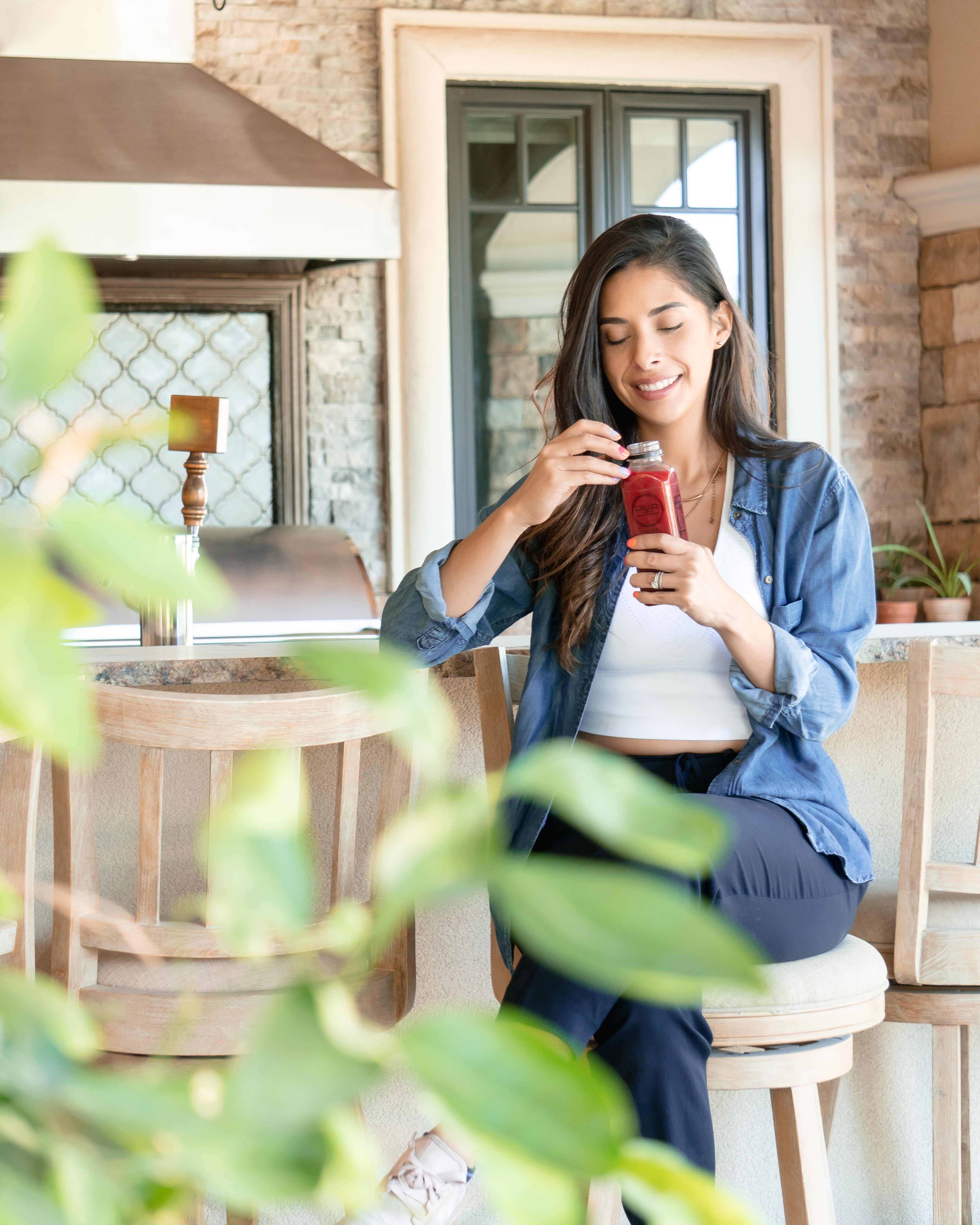 Woman enjoying a bottle of PUR Cold-Pressed juice while sitting in a bright, cozy outdoor area