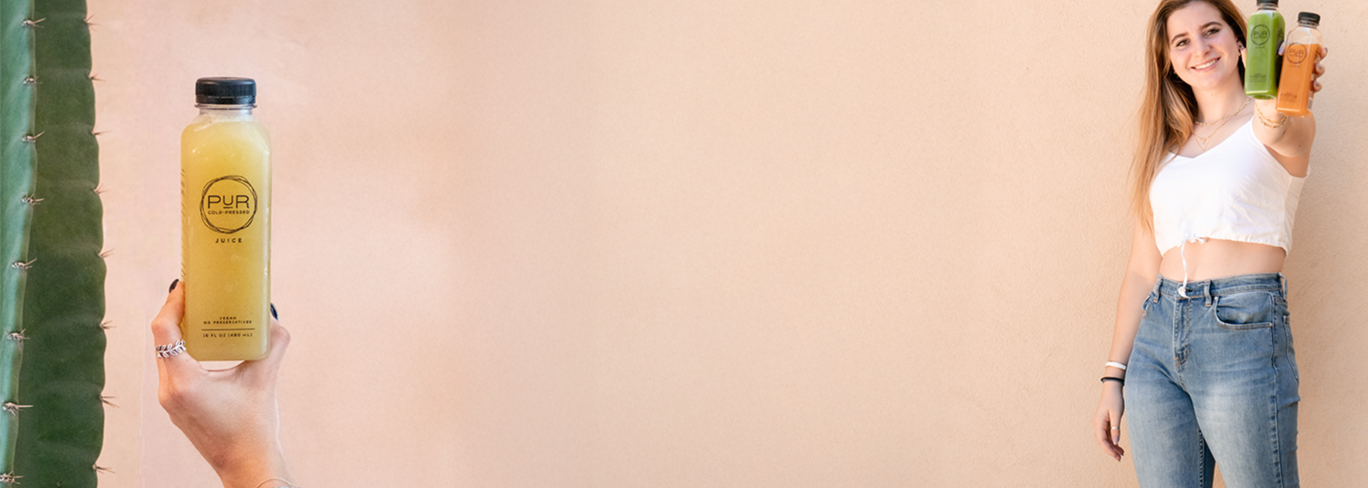 Person holding a bottle of PUR juice with a cactus plant on the left side.