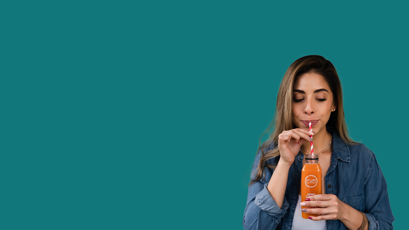 Woman drinking from a PUR sunny citrus bottle with a straw against a teal background