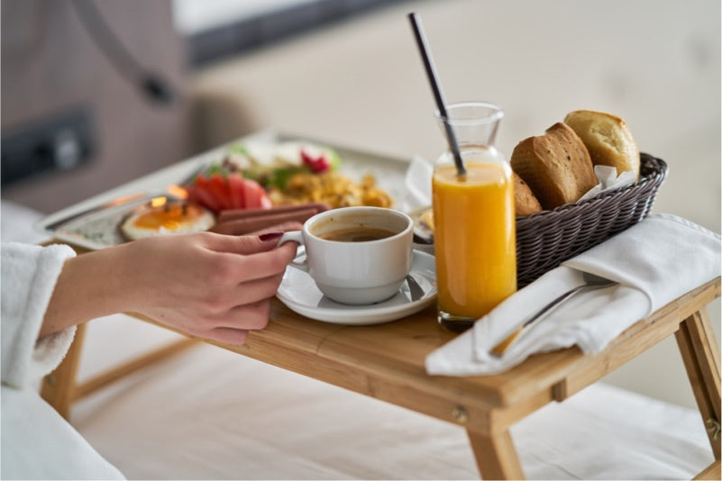 Room service breakfast tray with orange juice, coffee, and pastries in a cozy hotel setting.
