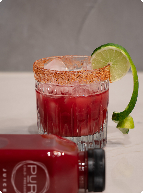 Glass of iced PUR red juice with tajín-style rim and lime twist—cocktail-style presentation.