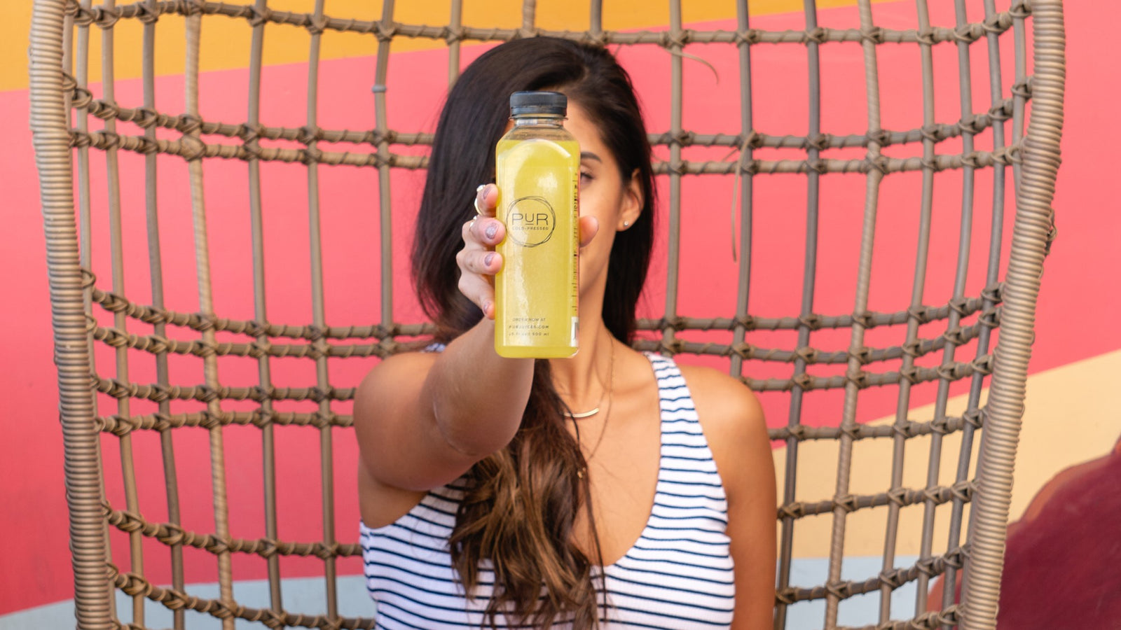 Woman holding a bottle of PUR juice in front of a colorful background